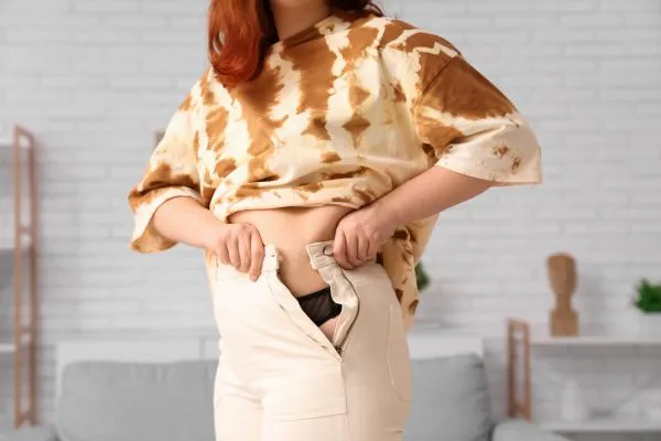 Image of woman trying to do her trousers up after pregnancy weight gain Coventry